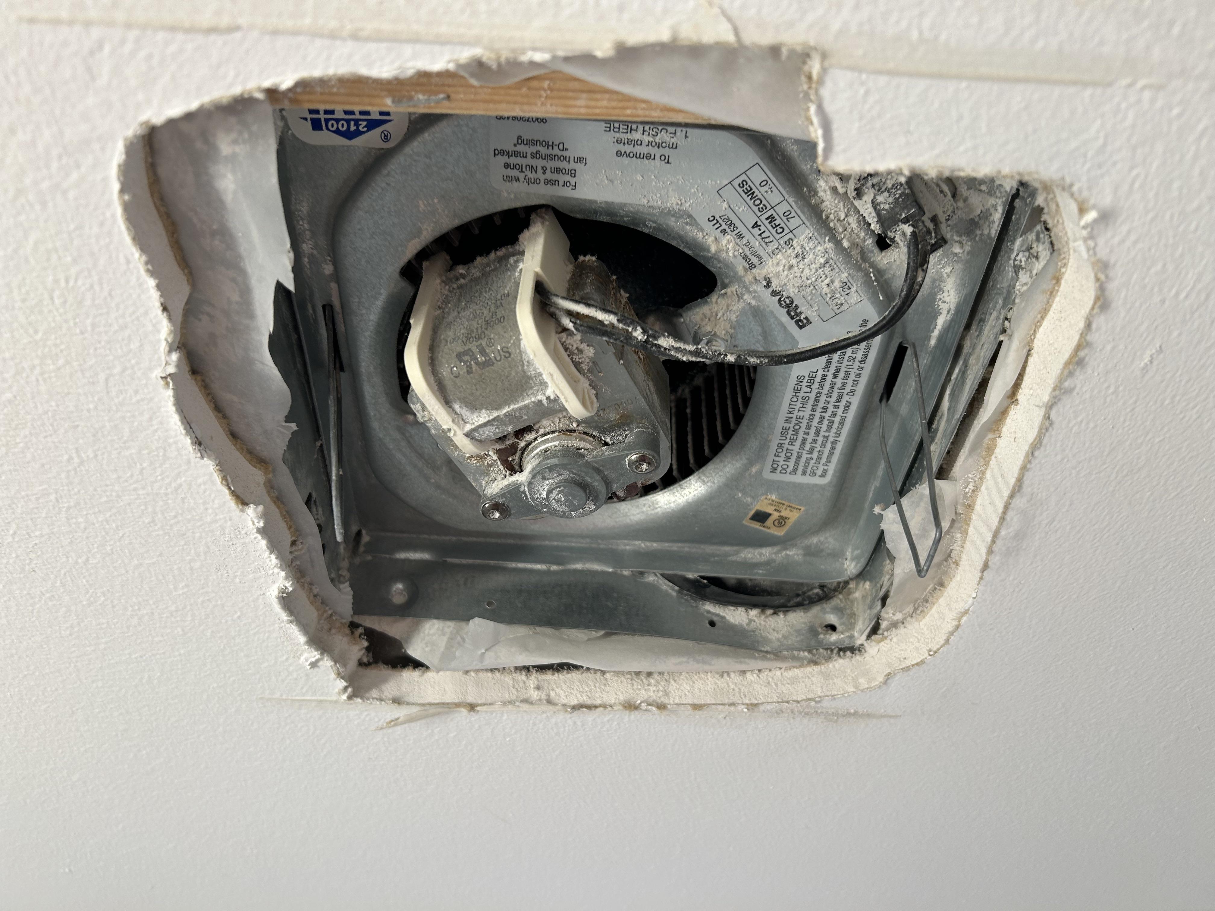 A bathroom ceiling exhaust fan grille removed and resting on a towel, showing heavy dust and lint buildup on the grille and fan housing