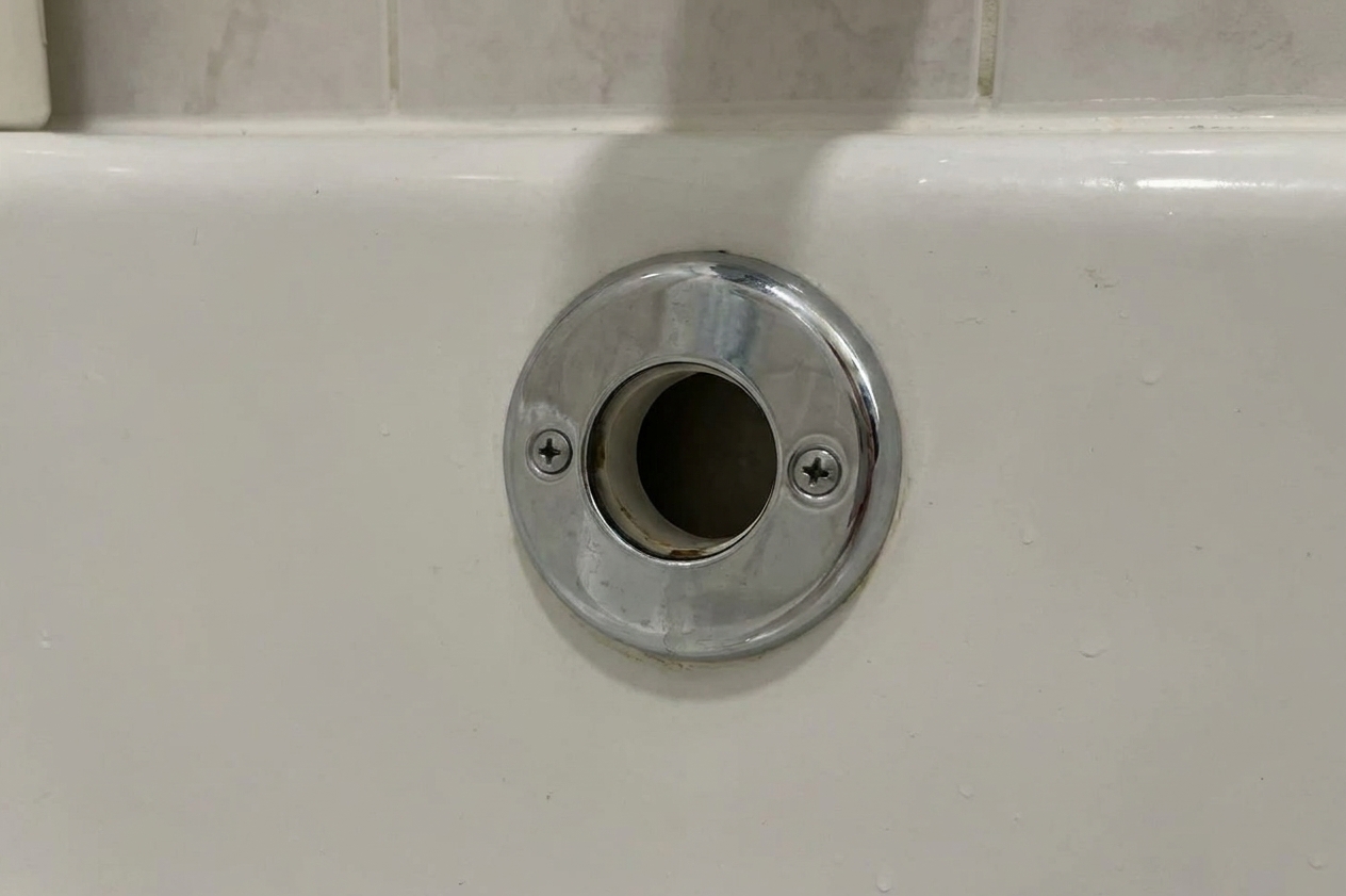 A bathtub overflow plate with two screws and the overflow opening visible behind it