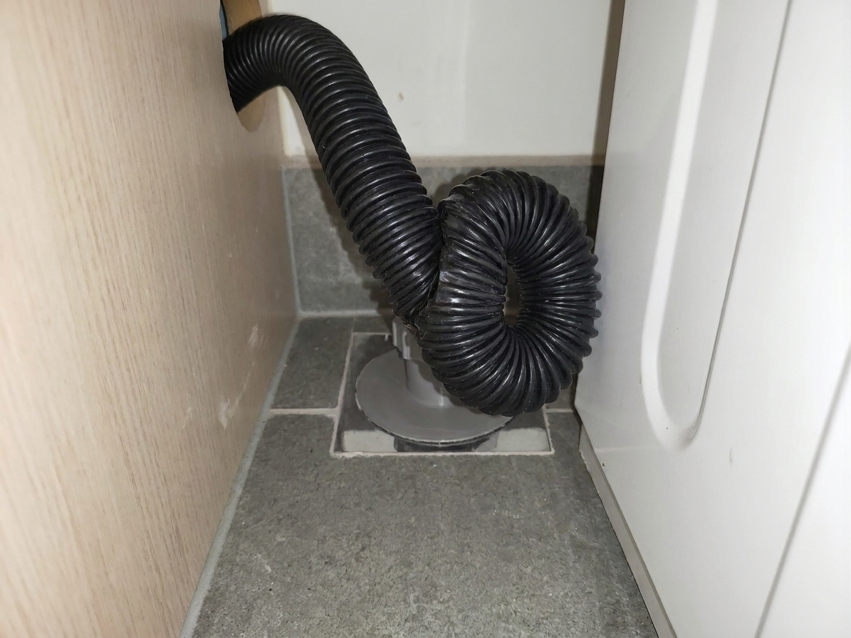 A black washing machine drain hose bent sharply behind the appliance, showing a visible kink where flow would be restricted
