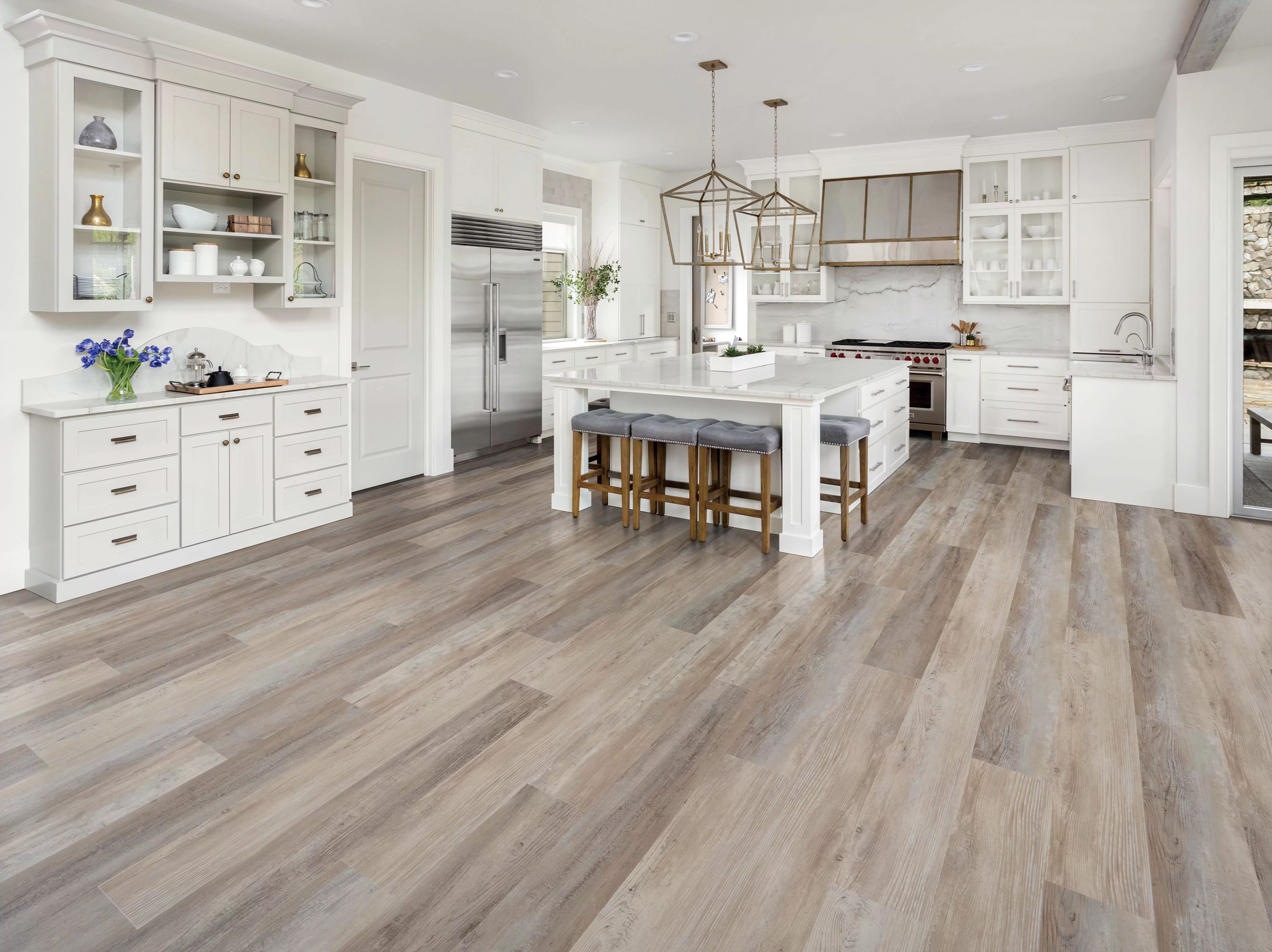 A bright kitchen with luxury vinyl plank flooring installed, showing realistic wood grain texture near a cabinet toe-kick