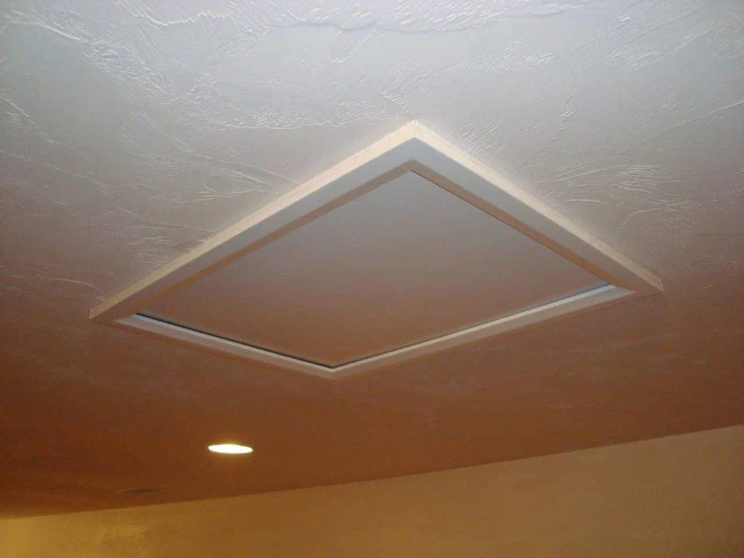 A ceiling attic hatch panel partially opened, showing the trim frame and the gap around the panel edge in a typical hallway ceiling