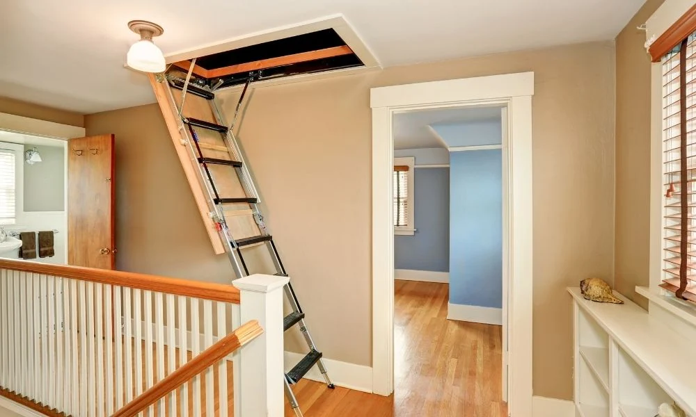 A ceiling-mounted attic pull-down stair unit partially opened, showing the wood frame around the opening and the folded ladder sections