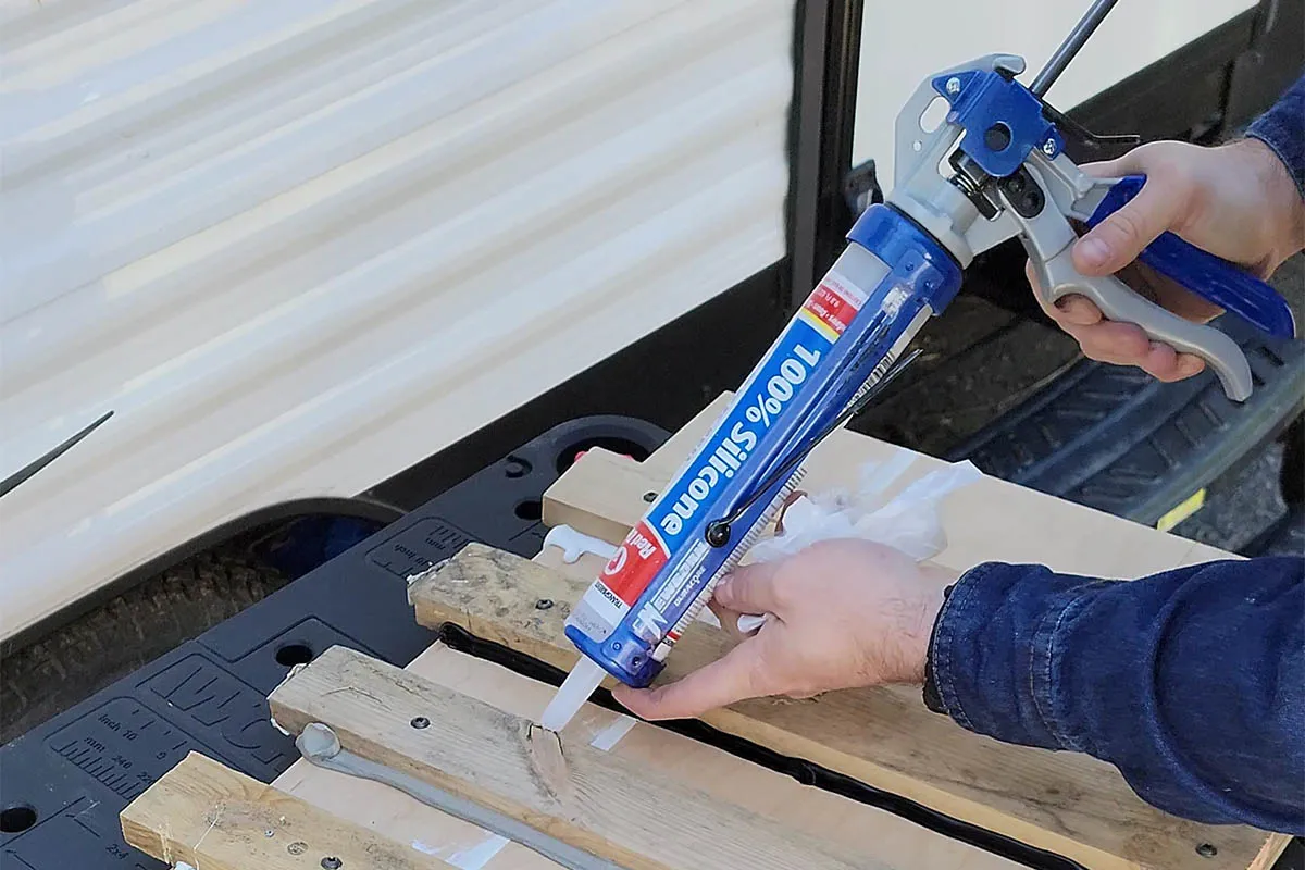 A close-up of a caulk gun applying a neat bead of exterior silicone caulk along the seam of a window trim board