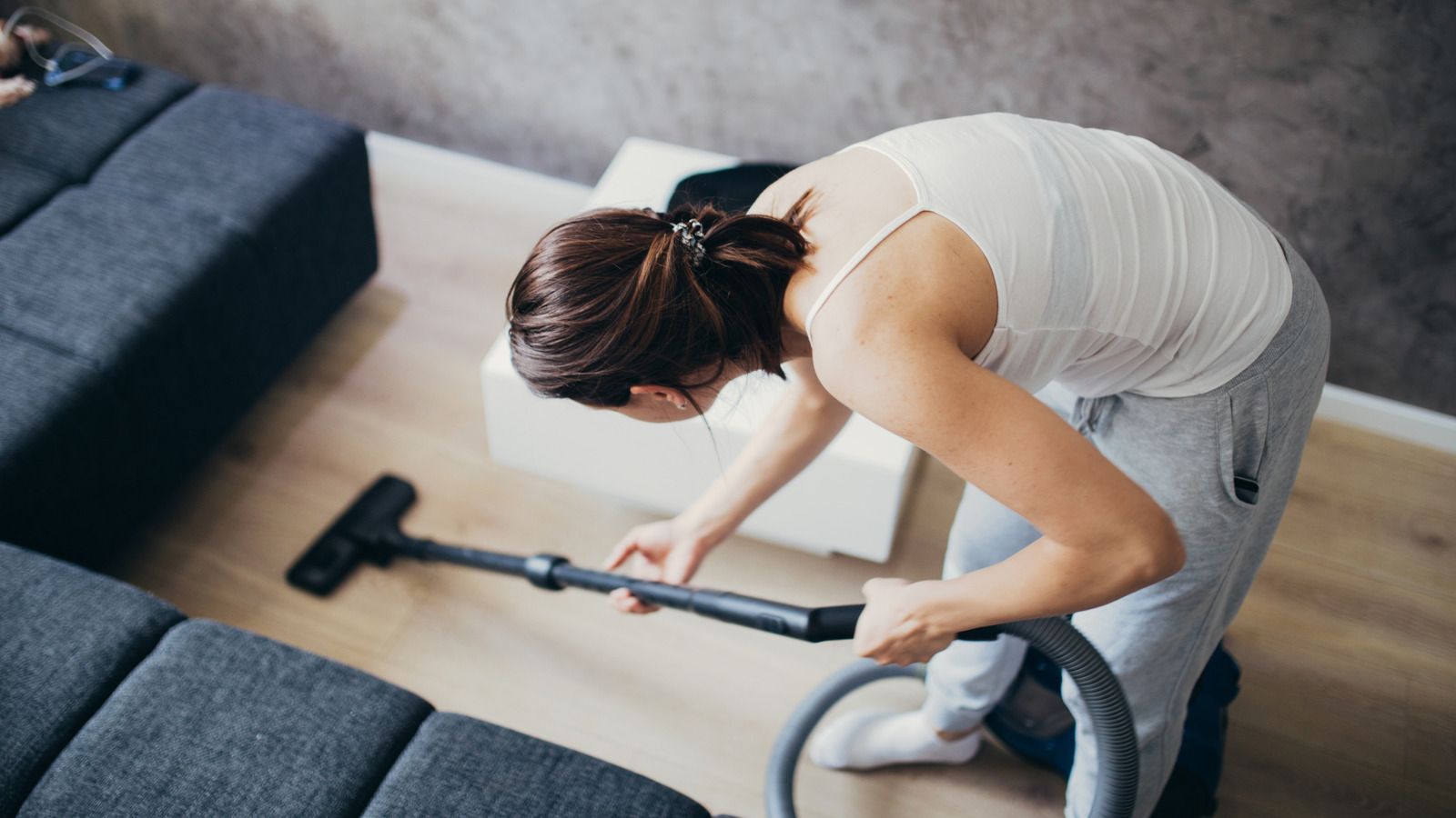A close-up photo of a homeowner vacuuming a wood-look vinyl plank floor with a soft floor attachment in a bright living room