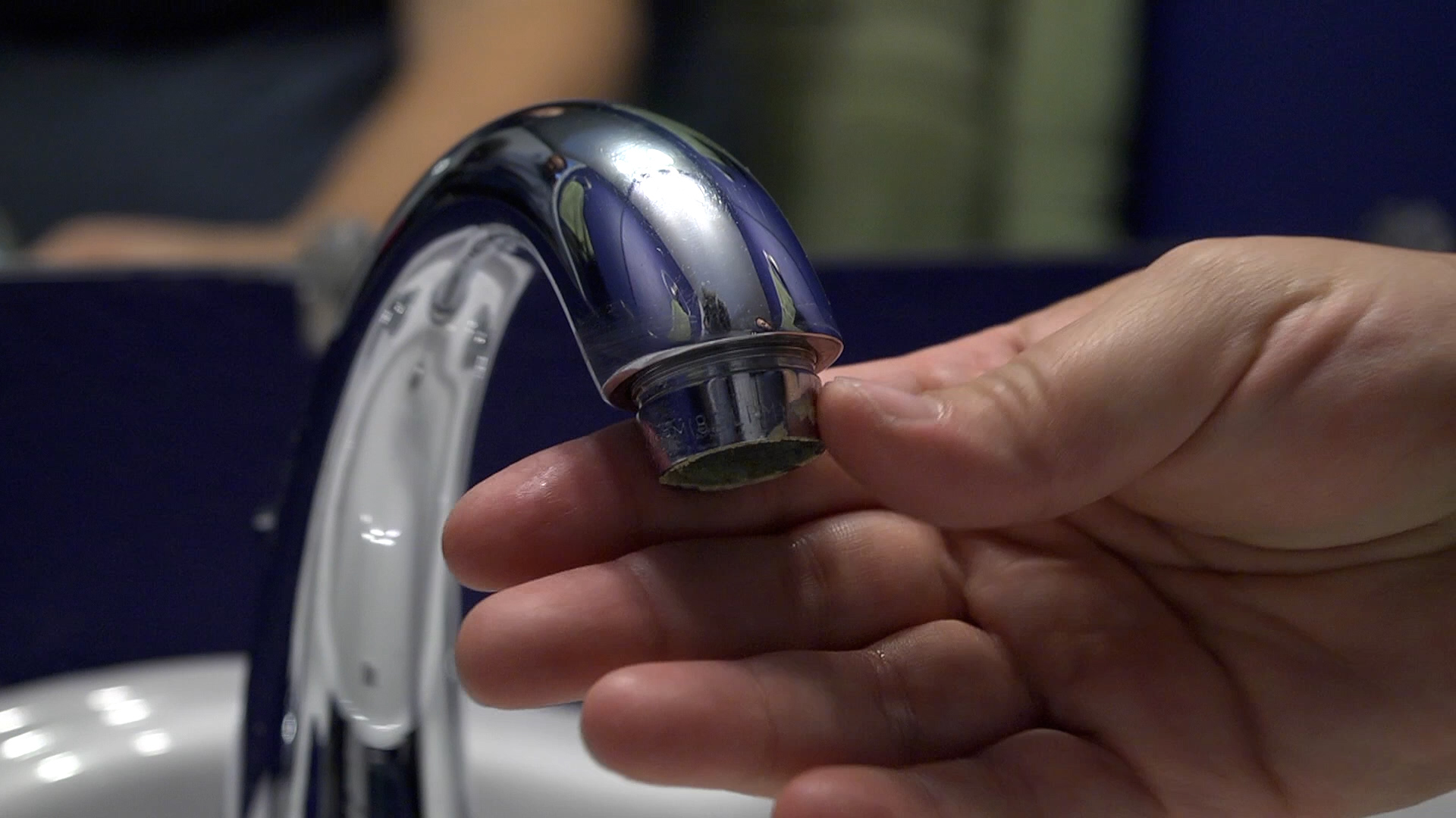 A close-up photo of hands unscrewing a metal faucet aerator from the tip of a bathroom sink faucet with a towel protecting the finish