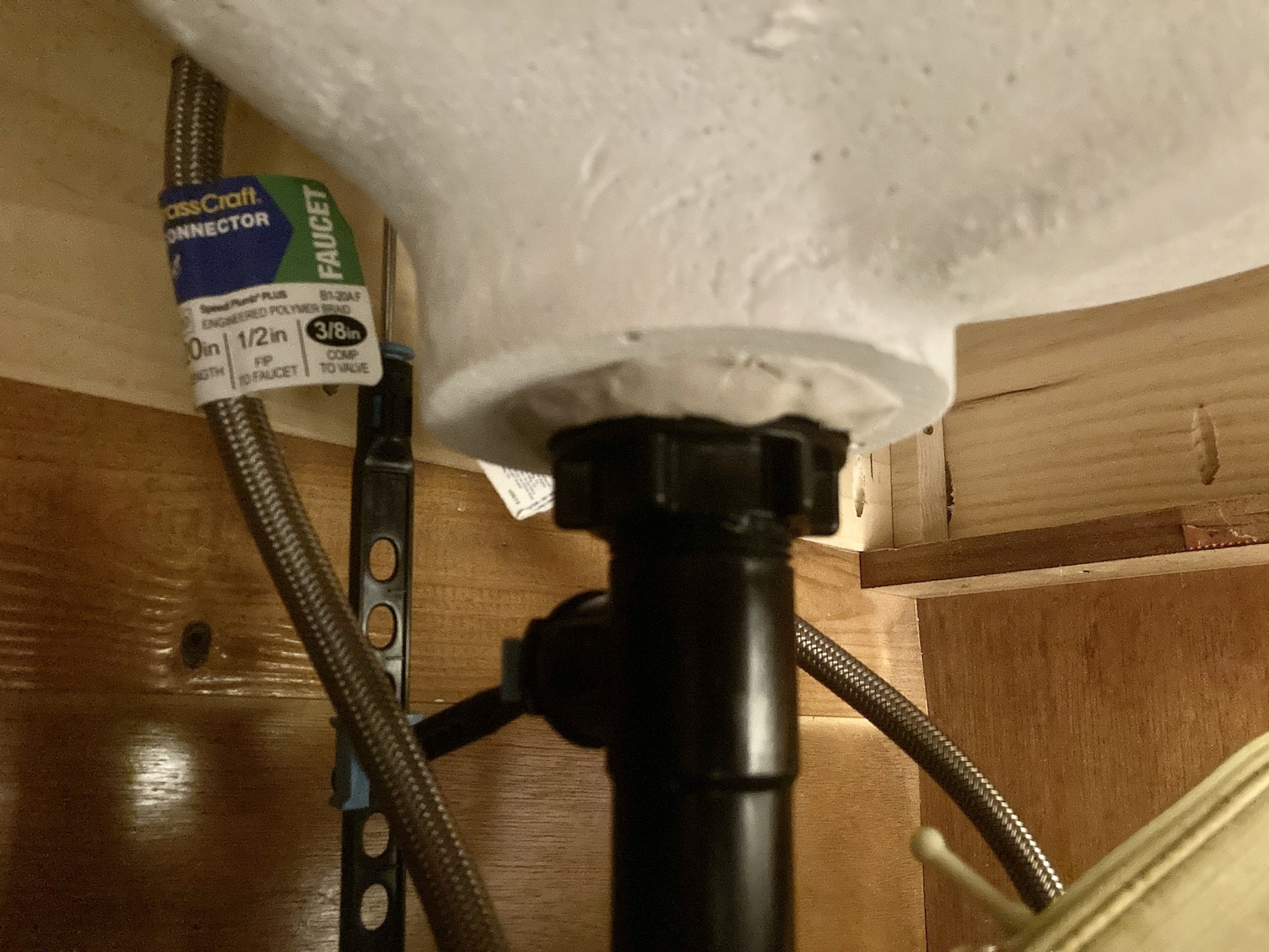 A close-up photo of water droplets forming under a bathroom sink drain tailpiece connection inside a vanity cabinet