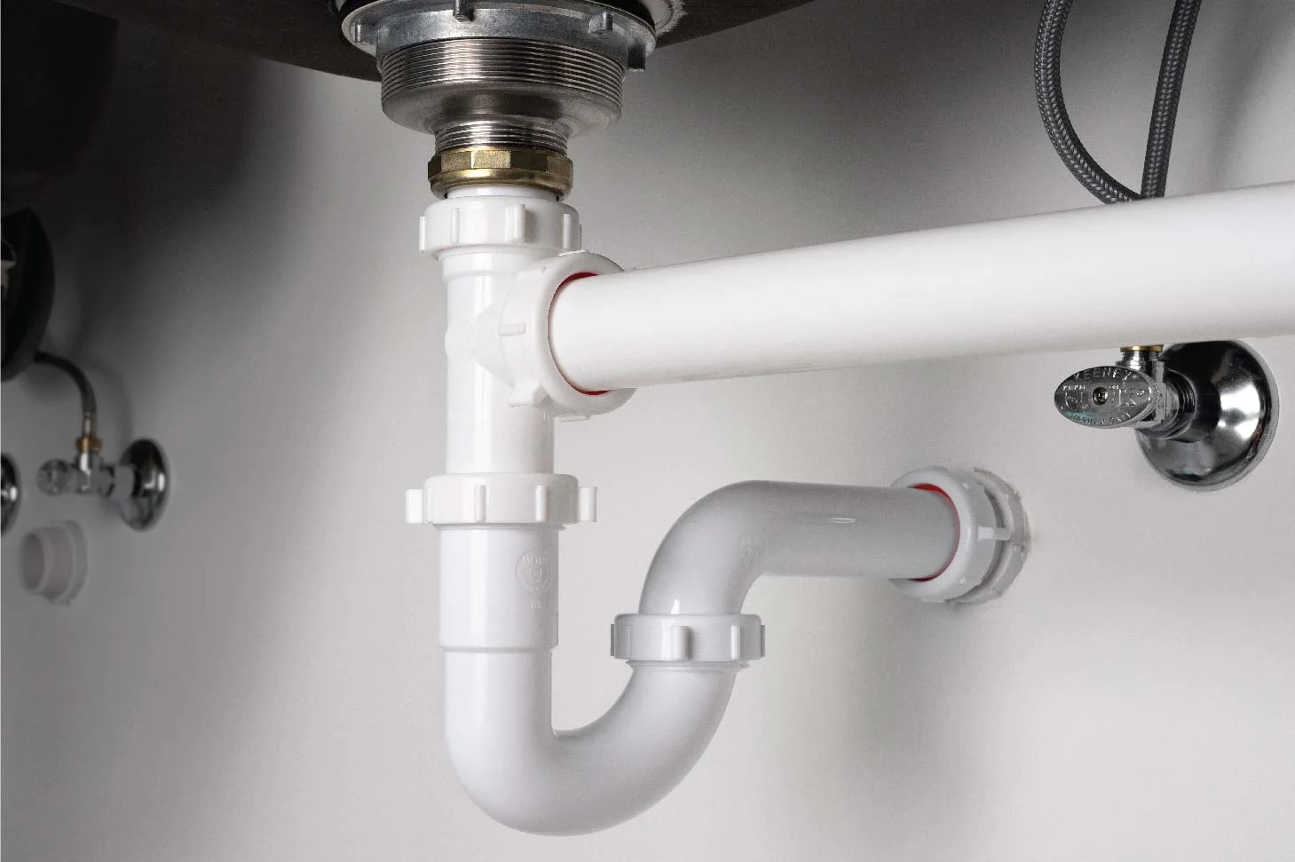 A close-up under a bathroom sink showing a white PVC p-trap and shutoff valves, with a flashlight beam aimed at a small drip point
