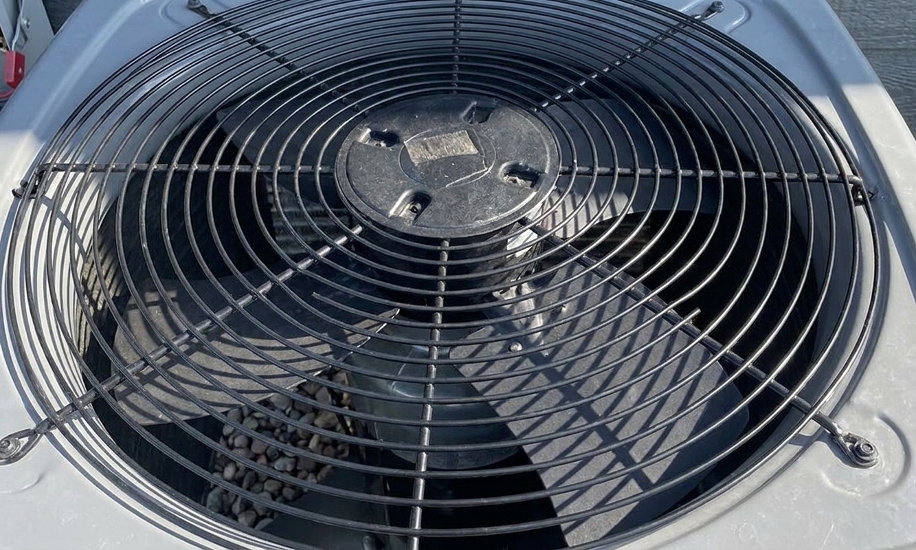 A close-up view down into an outdoor condenser showing the fan blades under the protective grille