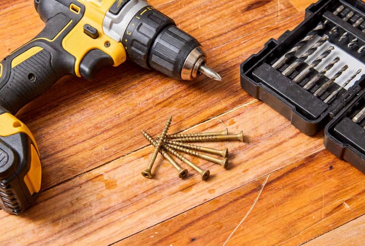 A cordless drill driver on a workbench next to a small pile of 2.5 inch deck screws and a drill bit set
