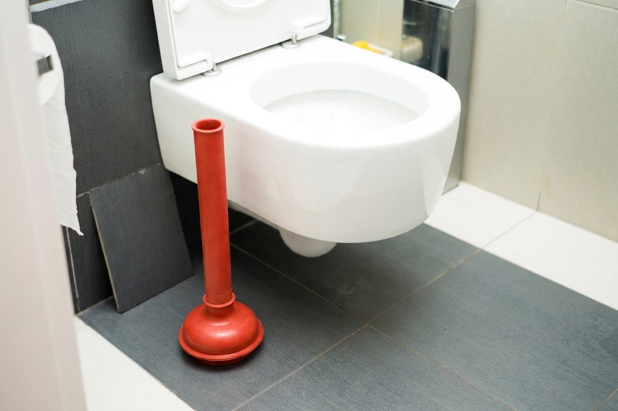 A flange-style toilet plunger with the rubber sleeve extended, positioned next to a toilet on a bathroom floor