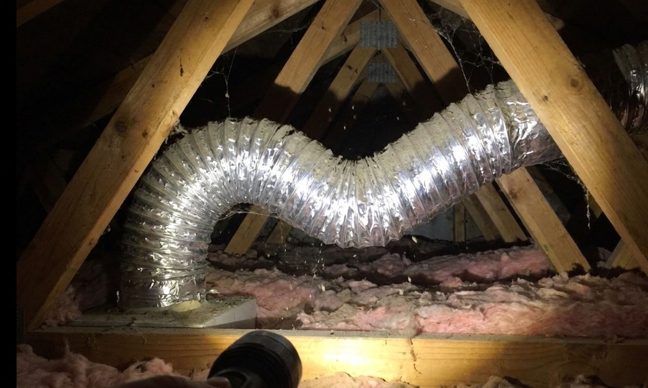A flexible aluminum bathroom exhaust duct in an attic with a visible kink and sag restricting airflow