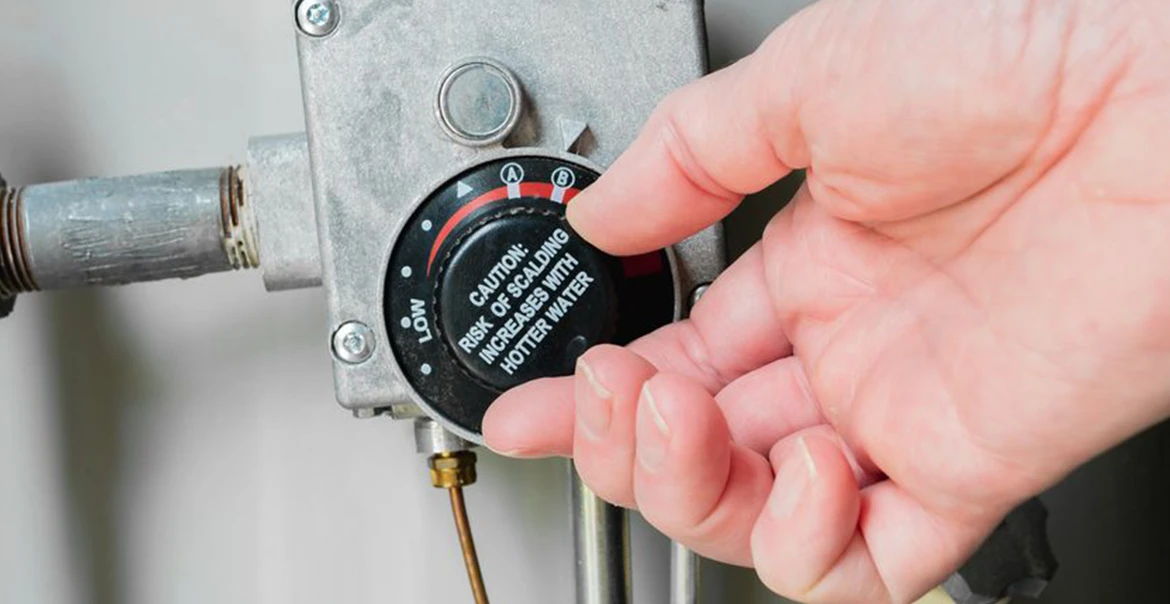 A homeowner adjusting a water heater temperature control dial on a tank-style unit