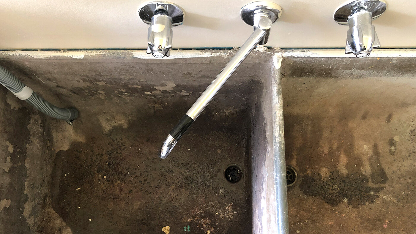 A laundry utility sink filled with standing water in a basement laundry room, with the drain strainer visible near the center