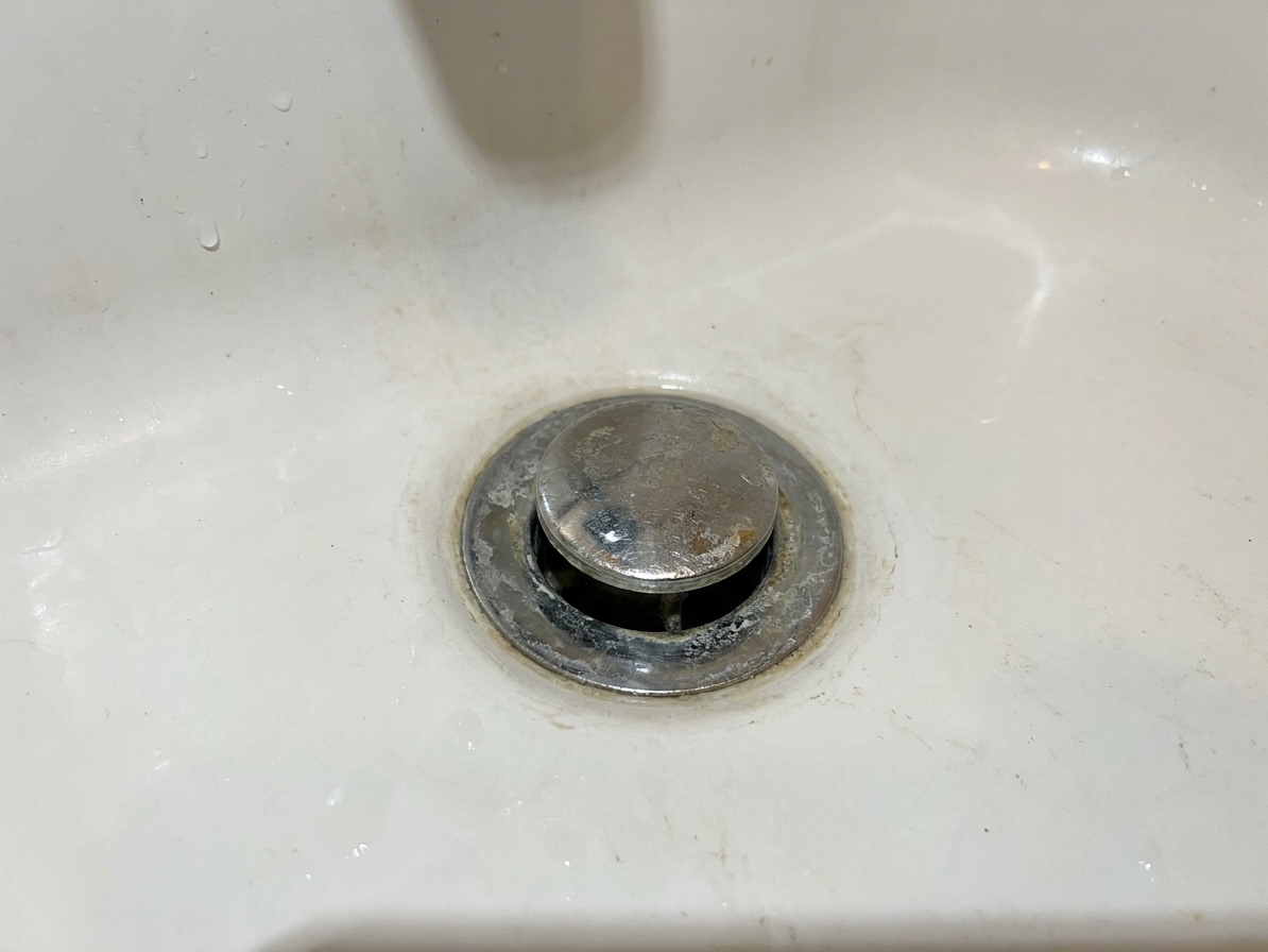 A photo of a bathtub drain area showing a metal stopper and the surrounding drain flange
