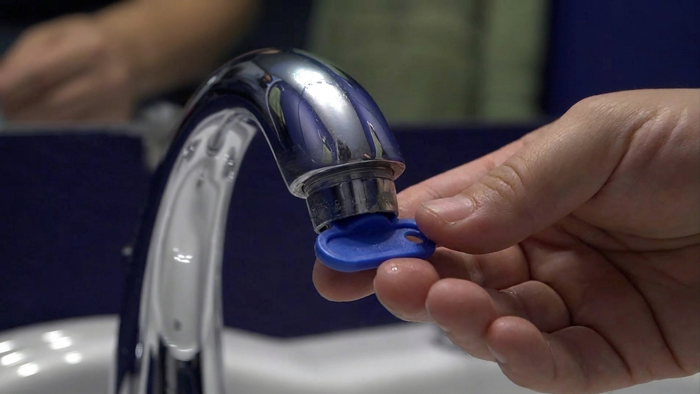 A photo of a plastic faucet aerator key tool held in a hand above a bathroom sink counter