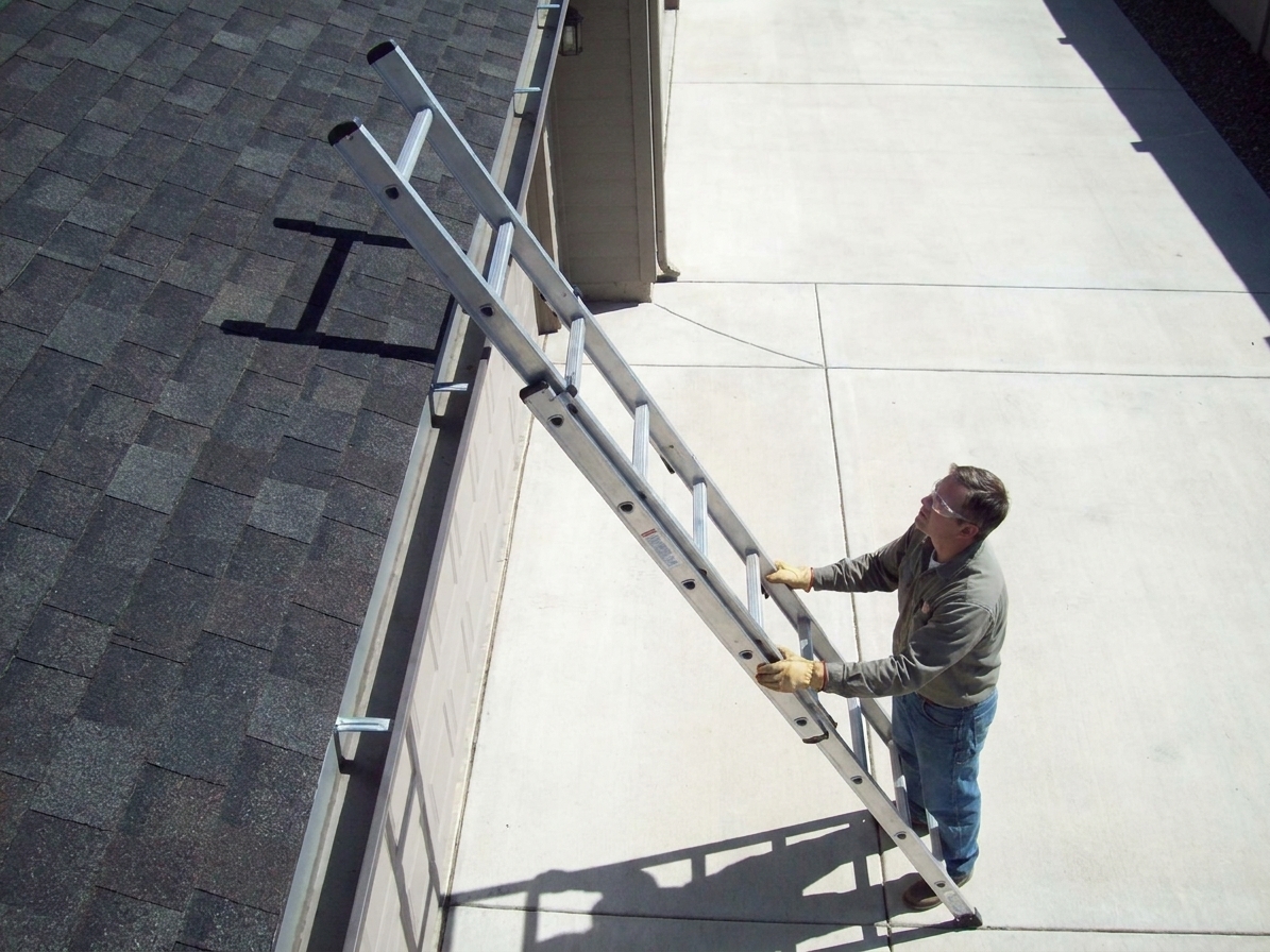 A properly positioned extension ladder extending above a roof edge on level ground, with a helper standing at the base