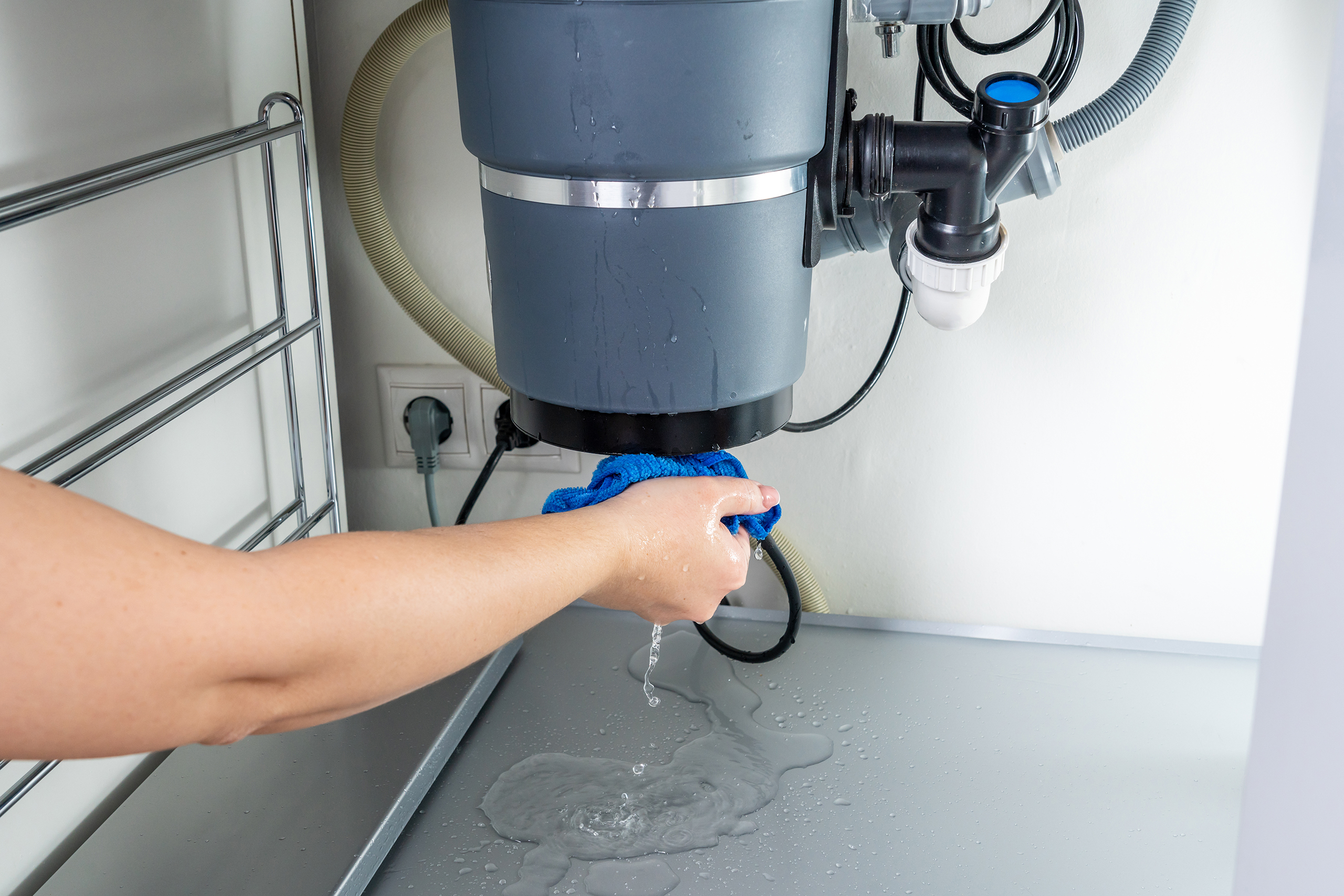 A real under-sink view with a garbage disposal installed, visible water droplets on the disposal body and a small puddle on the cabinet floor