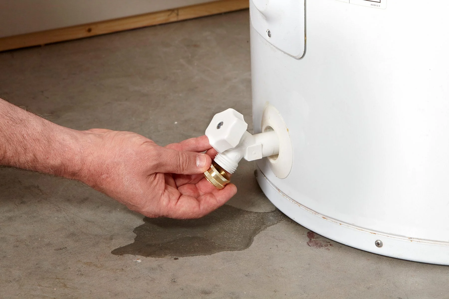 A real water heater in a basement with a small puddle of water on the concrete floor near the base, with visible copper pipes and a drain pan