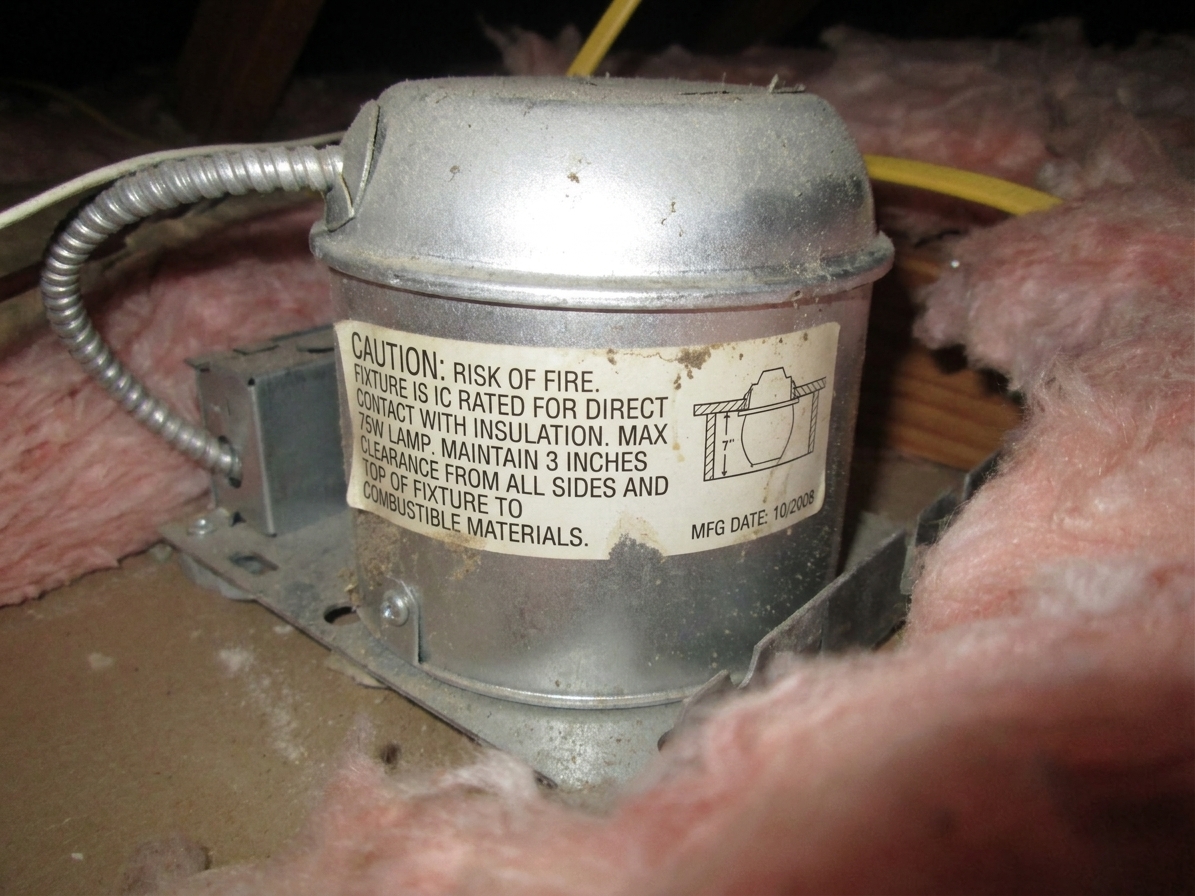 A recessed can light housing label in an attic showing the fixture rating and clearance information