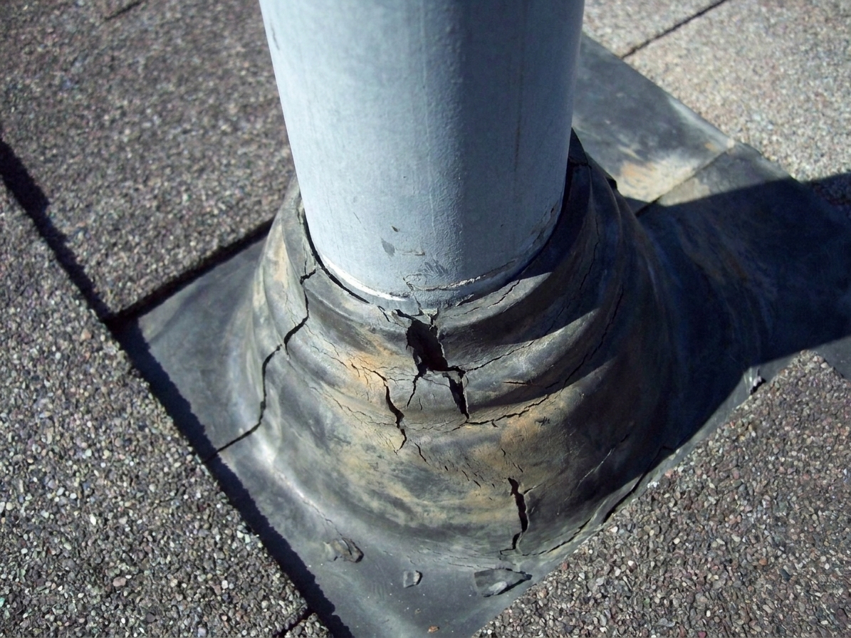 A roof plumbing vent pipe with a worn rubber flashing boot that shows visible cracking around the pipe opening