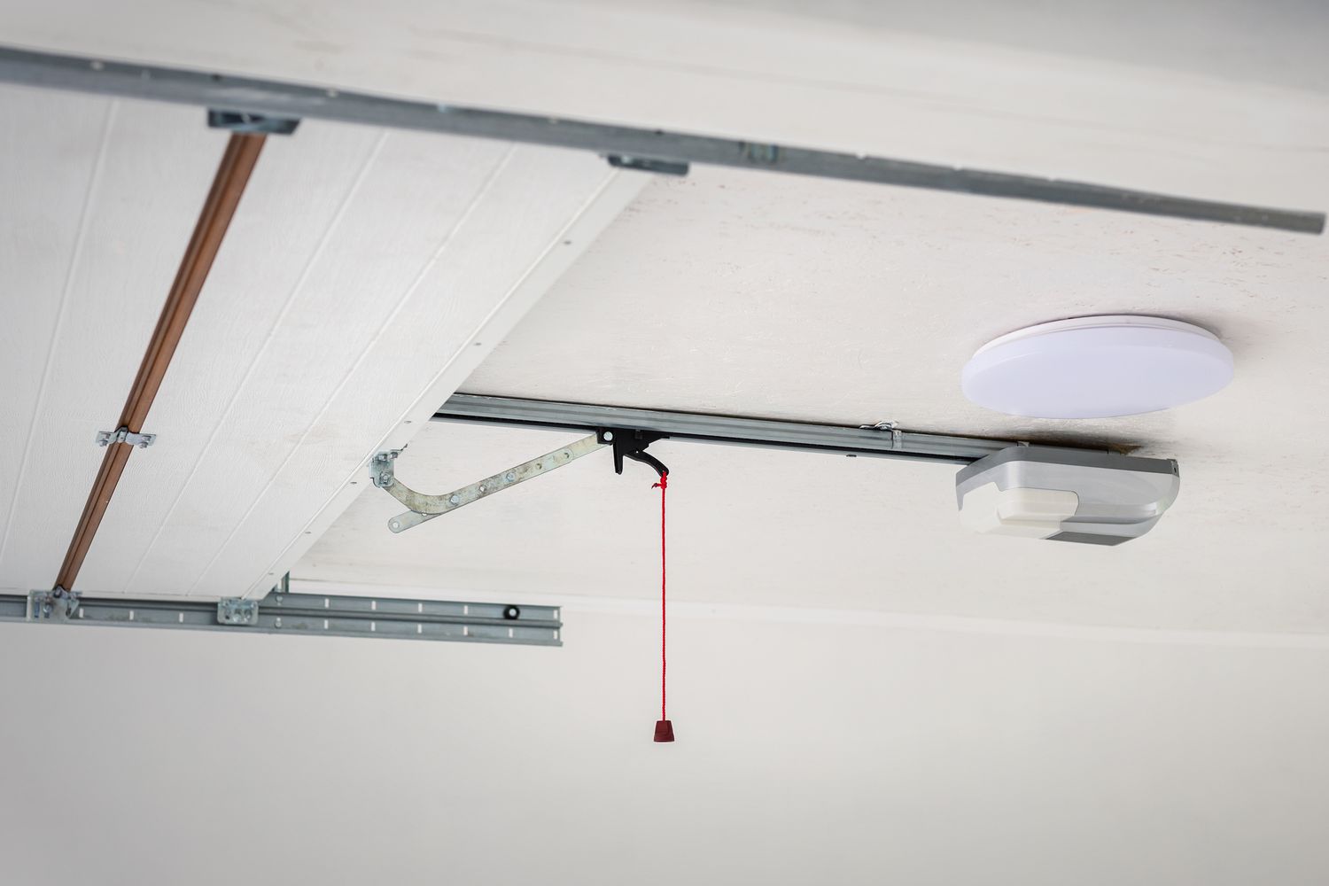 A standard garage door opener motor unit mounted to a garage ceiling with the light cover visible and the rail extending toward the door