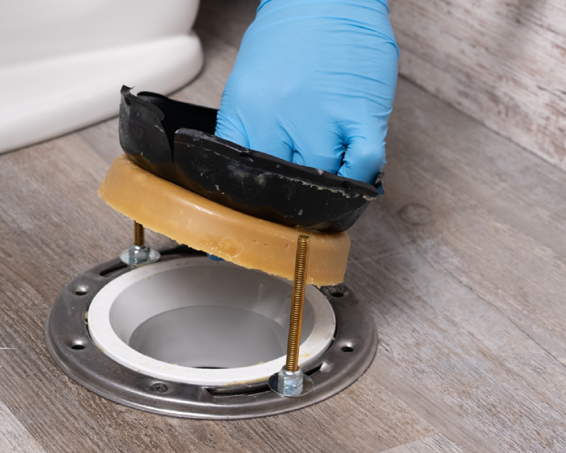 A toilet base area on tile with an adjustable wrench, a new wax ring package, and rubber gloves laid out on the floor