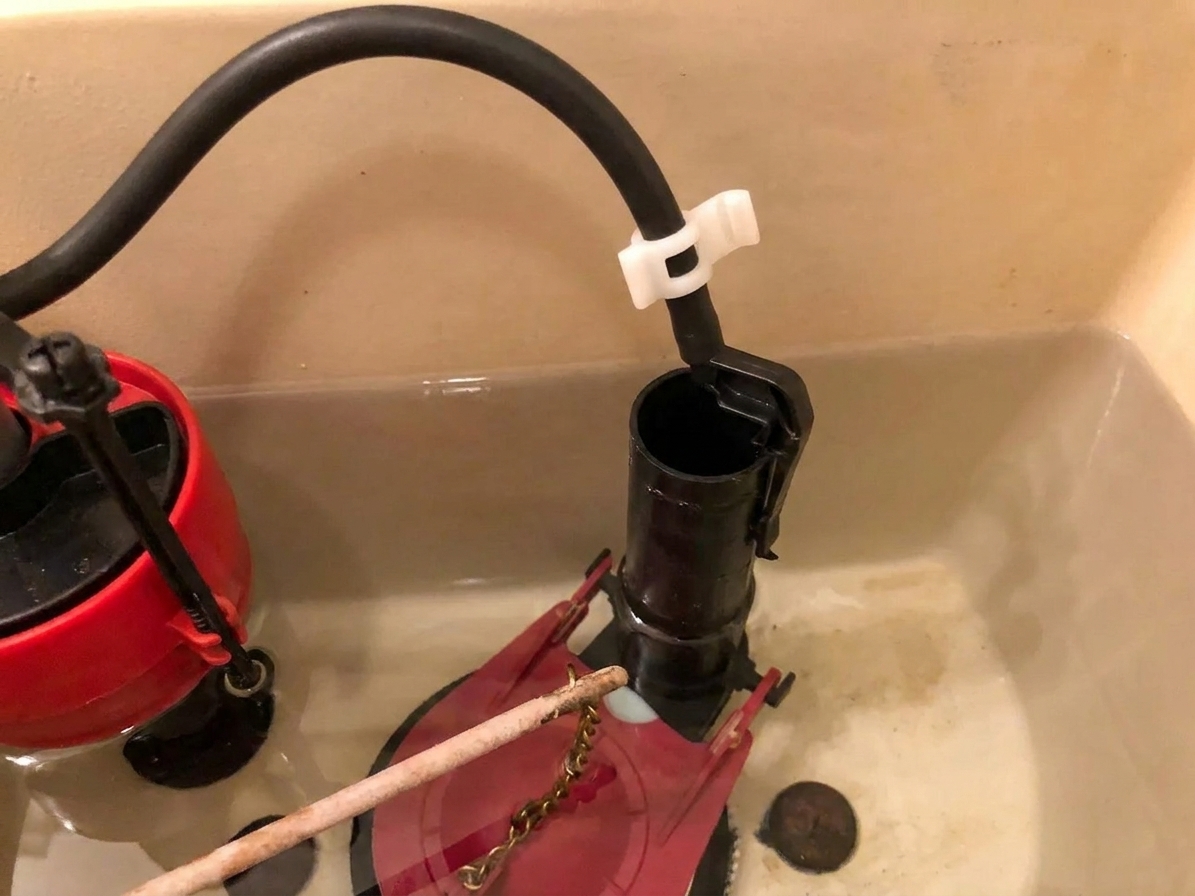 A toilet tank overflow tube with a refill tube held above the opening by a small plastic clip