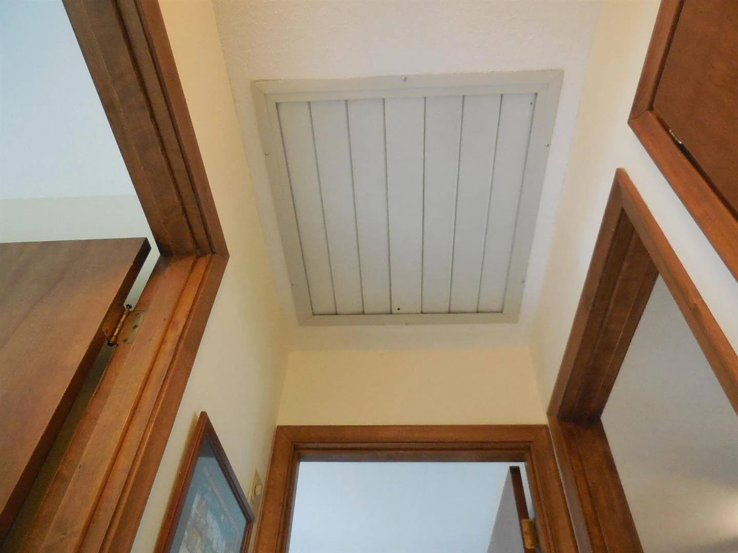 A whole-house fan ceiling grille with louvers, photographed from below in a hallway ceiling