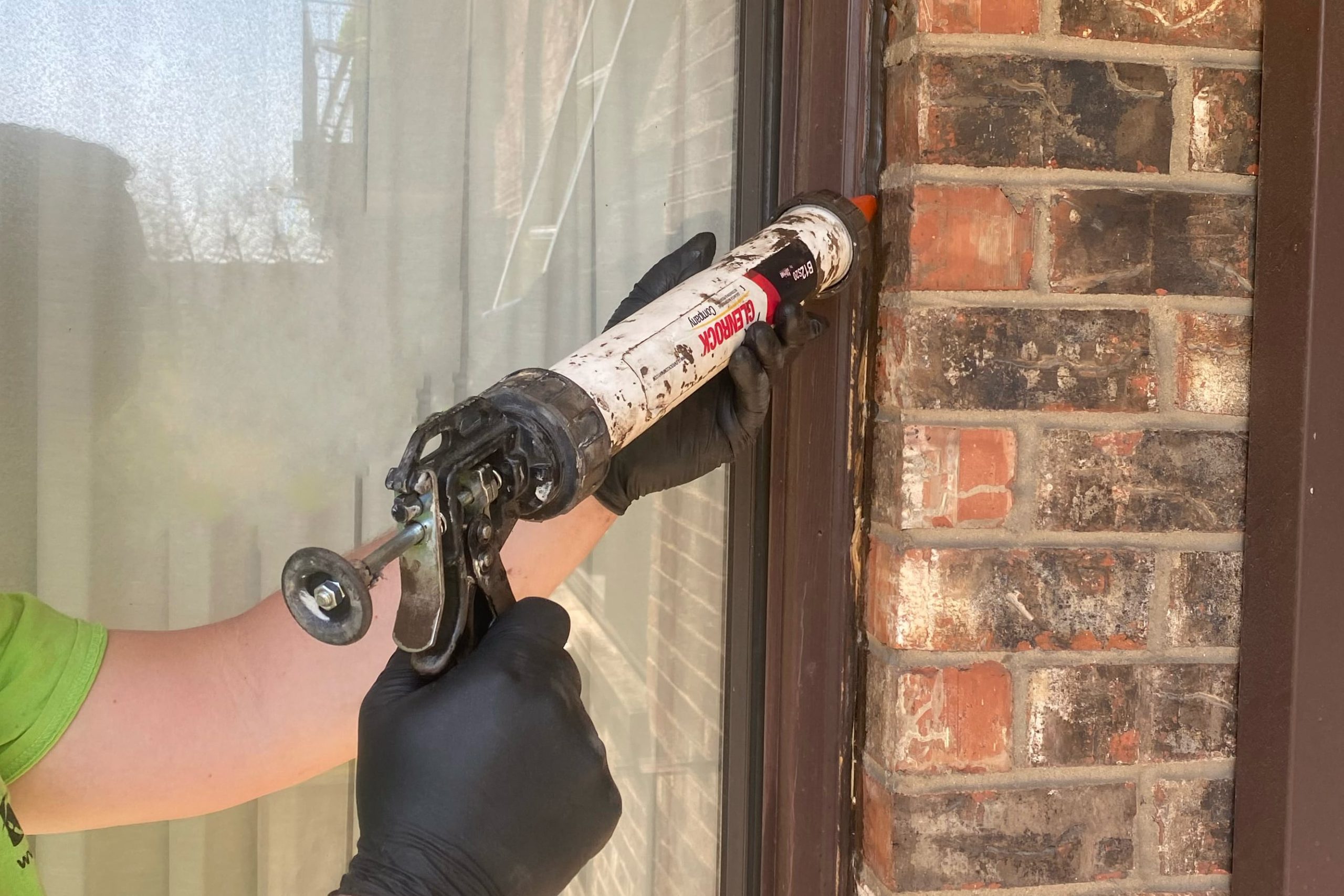 Close-up of a hand using a caulk gun to apply a neat bead of exterior caulk along the trim edge of a house window