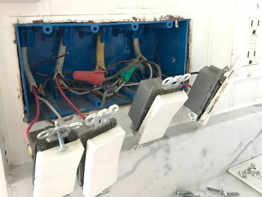 Close-up of a homeowner installing a pre-cut foam gasket behind a white electrical outlet cover plate on a painted wall