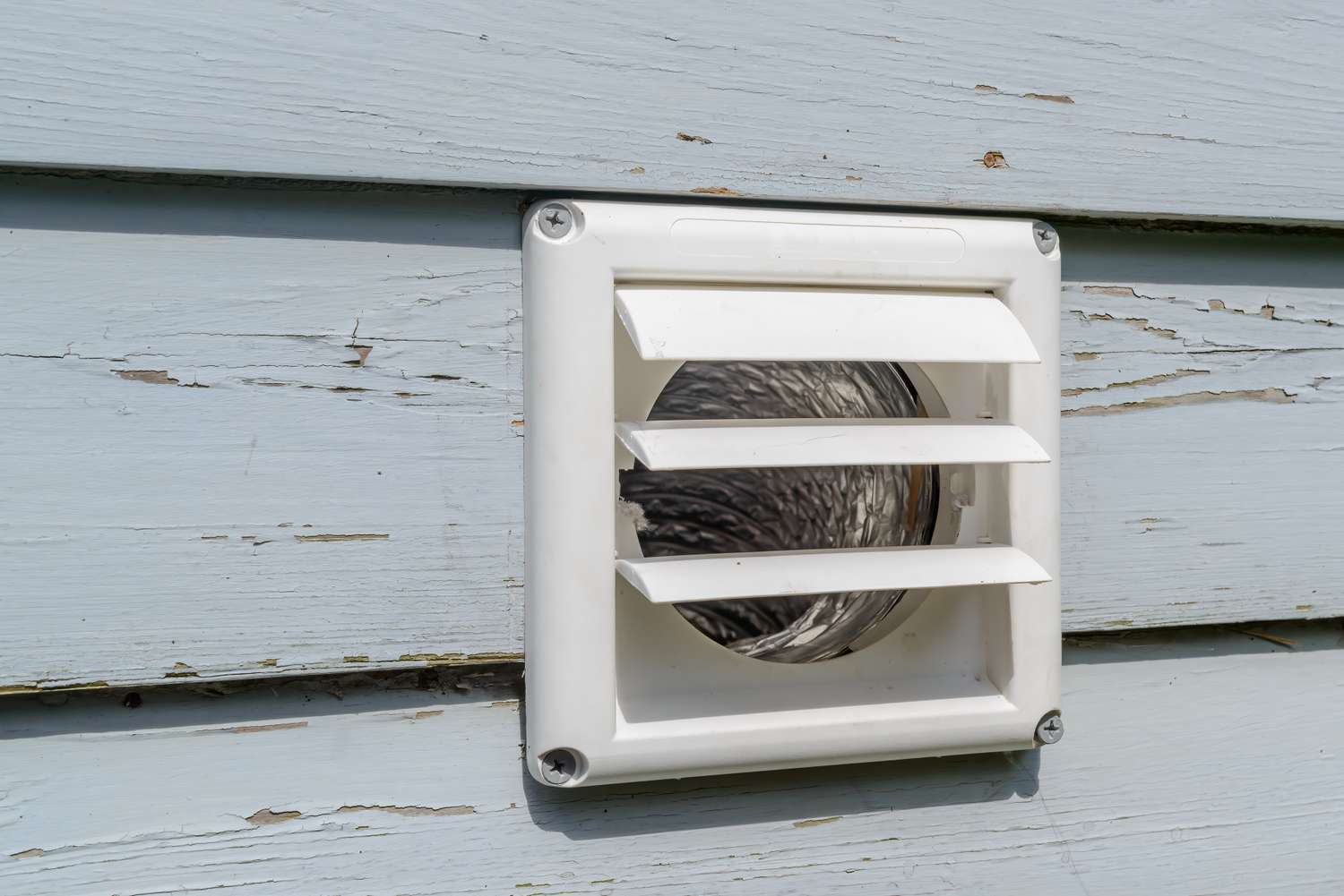 Close-up of an exterior dryer vent hood on a house wall with the flap partially open, showing lint buildup that needs cleaning