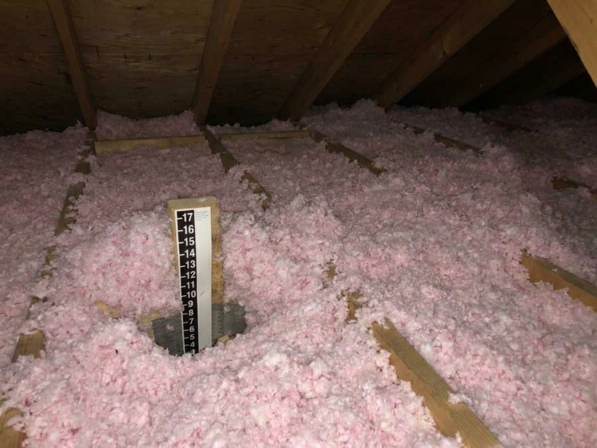 Loose-fill insulation spread across an attic floor around ceiling joists, with uneven depth visible near the eaves