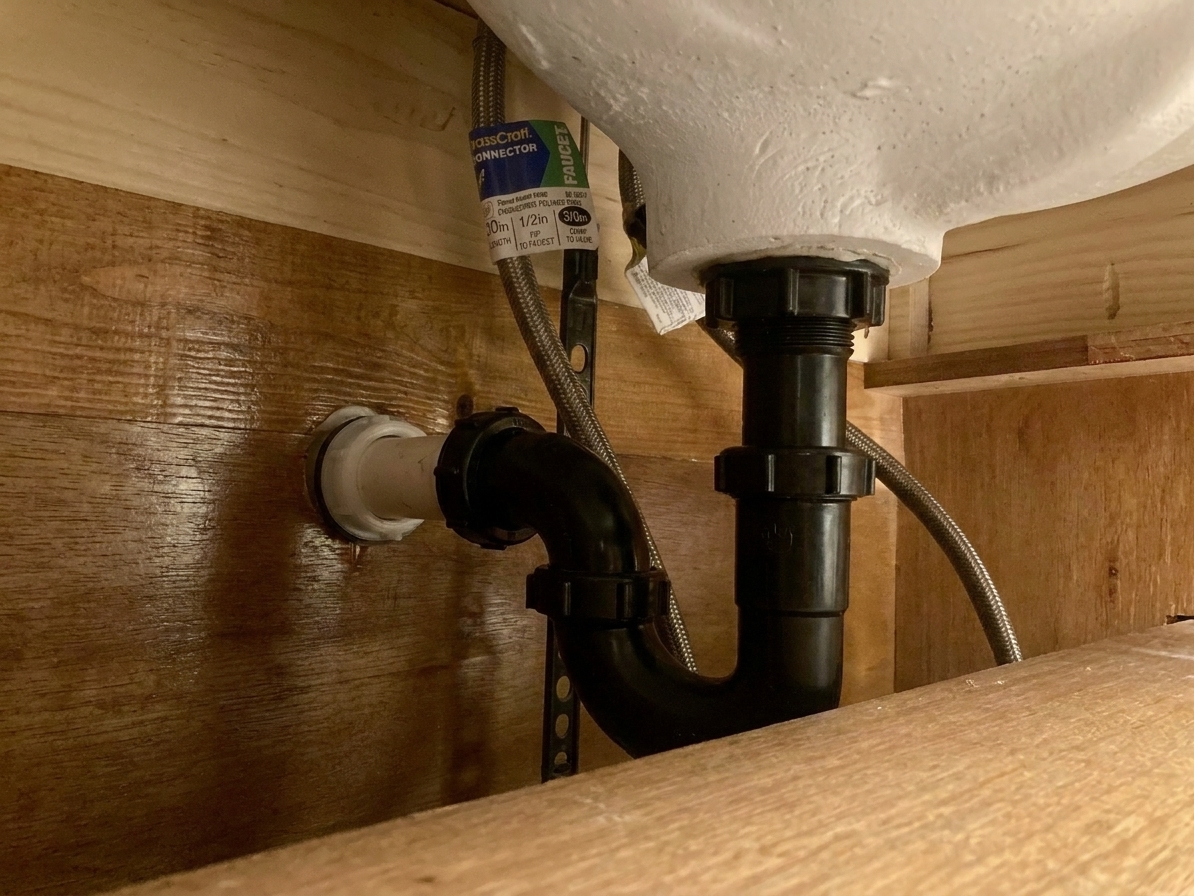 Under-sink view of a plastic P-trap aligned and hand-tightened to a bathroom sink drain tailpiece and wall stub-out
