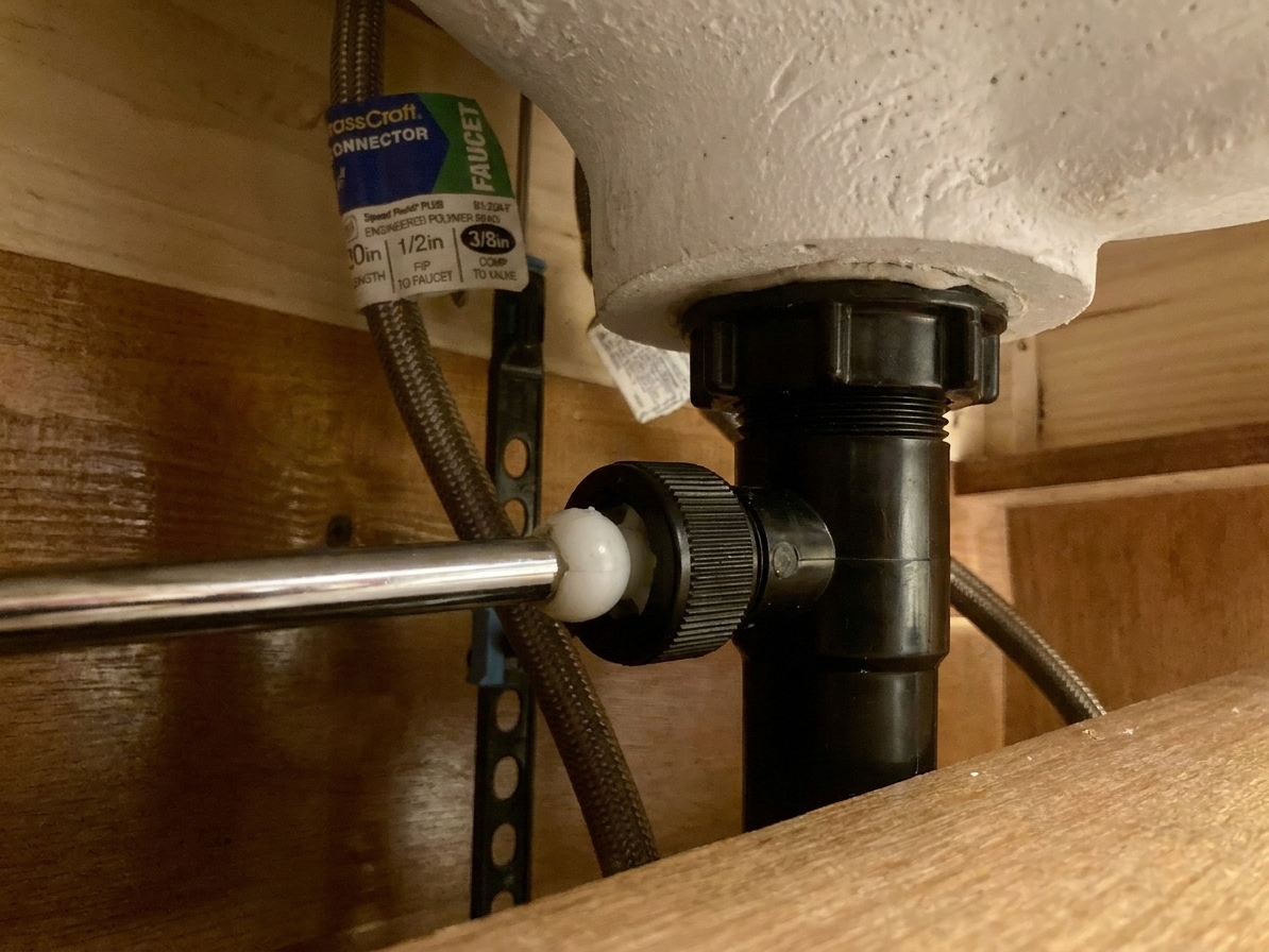 Under-sink view of a pop-up stopper pivot rod nut threaded into the back of a bathroom sink drain body